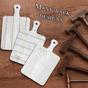 May include: Three white wooden cutting boards with different wood grain patterns. The boards have a handle on the top and are arranged on a brown wooden surface. The text "MANY BACK DESIGNS" is visible in the top right corner of the image.