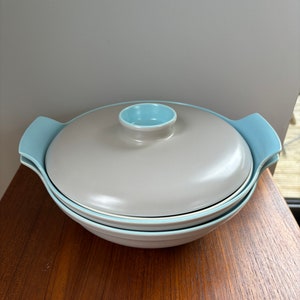 May include: A grey and light blue ceramic serving bowl with a lid. The bowl has a rounded shape and two handles on the sides. The lid has a small knob on top.