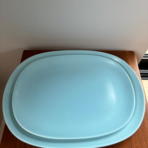 May include: Two light blue oval ceramic serving platters, one nested inside the other, on a wooden surface.