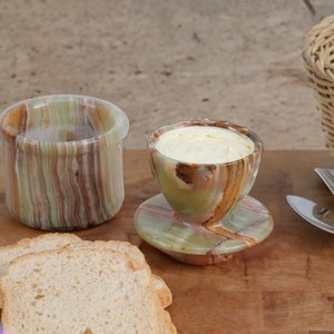 May include: A set of two green and brown marble butter dishes. The smaller dish has a lid and is filled with butter. The larger dish is empty and has a smooth, polished surface.
