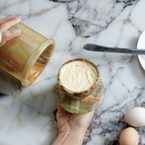 May include: A green and brown marble butter dish with a lid, filled with butter, on a green and brown marble coaster.