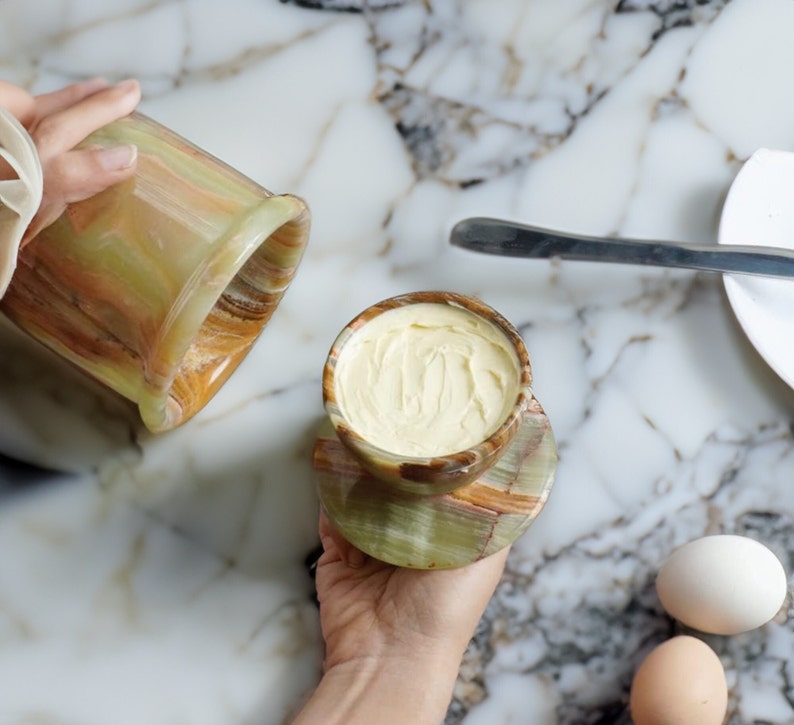 May include: A green and brown marble butter dish with a lid, filled with butter, on a green and brown marble coaster.