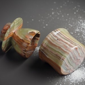 May include: Two green, brown, and white striped onyx salt and pepper shakers. The salt shaker is a round, squat shape, while the pepper shaker is a taller, more conical shape.