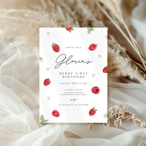 Puede incluir: Una tarjeta de invitación blanca con un nombre escrito a mano "Gloria's" y el texto "Berry First Birthday" con una fecha y hora. La tarjeta está decorada con frambuesas rojas y hojas verdes.