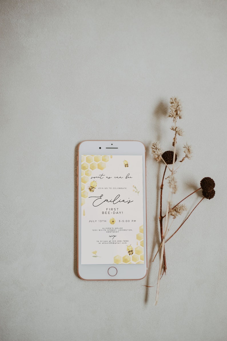 Op de afbeelding: Een smartphone die een gele en witte uitnodiging met een bijenmotief weergeeft. De uitnodiging luidt "Sweet as can bee" en "Emilia's First Bee-Day!" met een datum en tijd voor het evenement.