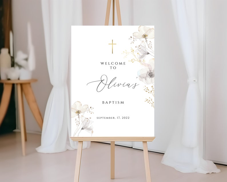 Puede incluir: Un letrero blanco sobre un caballete de madera con el texto "Welcome to Olivia's Baptism" en escritura elegante. Una cruz dorada y detalles florales adornan la parte superior y los lados. La fecha "September 17, 2022" se muestra en la parte inferior.