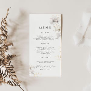 Puede incluir: Una tarjeta de men&uacute; blanca con un dise&ntilde;o floral y detalles dorados. El men&uacute; incluye ensaladas, plato principal, postre y el texto "Natasha's bridal shower May 18, 2022".