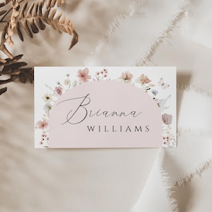 May include: A white card with a pink floral border and a pink circle in the center. The text "Brianna WILLIAMS" is written in black cursive inside the circle.