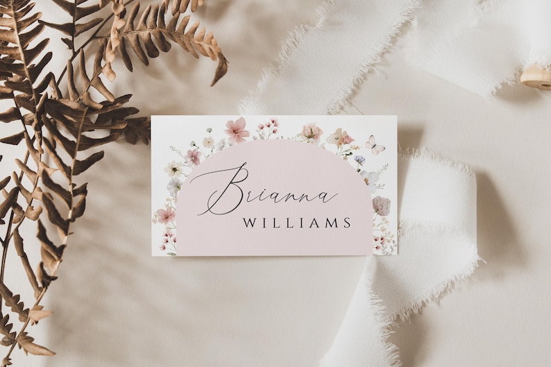 May include: A white card with a pink floral border and a pink circle in the center. The text "Brianna WILLIAMS" is written in black cursive inside the circle.
