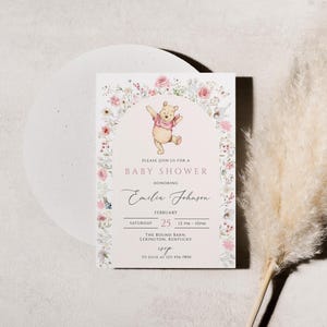 Pode incluir: Um convite para ch&aacute; de beb&eacute; com uma ilustra&ccedil;&atilde;o de Winnie the Pooh. O convite tem um design de arco floral com o texto "Baby Shower" e detalhes para o ch&aacute; de beb&eacute; de Emilia Johnson. O convite est&aacute; em um fundo branco.