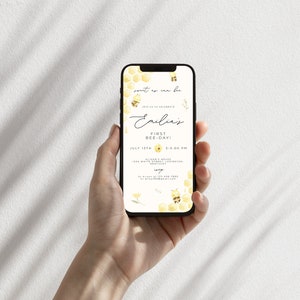 Op de afbeelding: Een smartphone die een uitnodiging voor een eerste verjaardagsfeestje met een bijen-thema voor Emilia laat zien. De uitnodiging heeft een honingraatpatroon, bijen en de tekst "sout ex cen bu" en "Vier met ons Emilias eerste bijendag!" De uitnodiging bevat ook de datum, tijd en locatie van het feest.