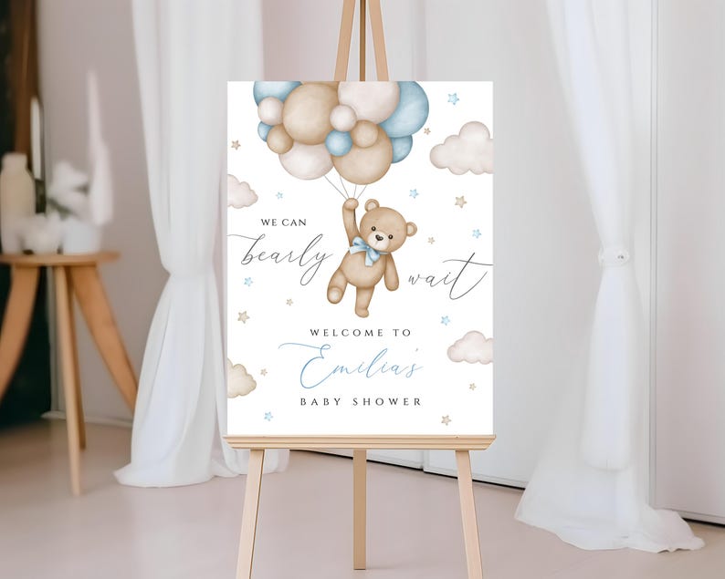 May include: A white welcome sign with a teddy bear holding balloons. The sign says "We can bearly wait" and "Welcome to Emilias Baby Shower".