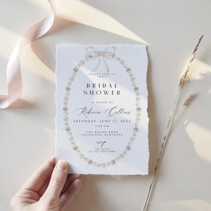 May include: A white bridal shower invitation with a pearl necklace design. The invitation reads "Please join us for a Bridal Shower in honour of Rebecca Collins, Saturday, June 11, 2022, 1:00 PM, The Round Barn, Lexington, Kentucky."