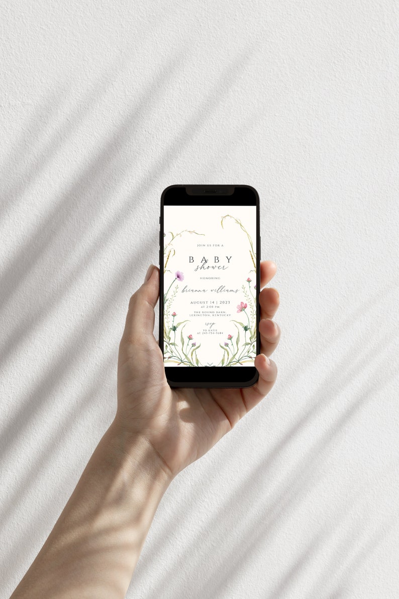 May include: A smartphone displaying a baby shower invitation with a floral design. The invitation reads "Join us for a Baby Shower honoring Brianna Williams, August 14, 2023, at 2:00 PM, The Boling Barn, 12345 Somewhere, Anywhere".
