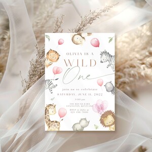 May include: A white invitation card with a pink and brown watercolor illustration of animals. The text on the card reads "Olivia is a Wild One" and includes details for a birthday party.