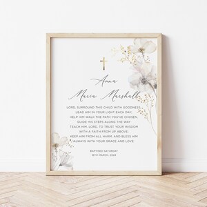 May include: A white and gold floral print with a cross and the text "Anna Maria Marshall" and a baptism date. The text reads "Lord, surround this child with goodness, lead him in your light each day: help him walk the path you've chosen, guide his steps along the way teach him, Lord, to trust your wisdom with a faith from up above keep him from all harm, and bless him always with your grace and love. Baptised Saturday 16th March, 2024."