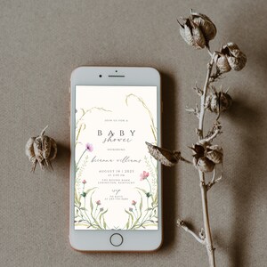 May include: A digital invitation on a smartphone screen for a baby shower. The invitation features a floral design with pink flowers and green leaves. The text reads "Join us for a baby shower honoring Brianna Williams, August 14, 2023 at 2:00 PM, The Round Barn, Lexington, Kentucky. RSVP to Katie at 245-754-5684."