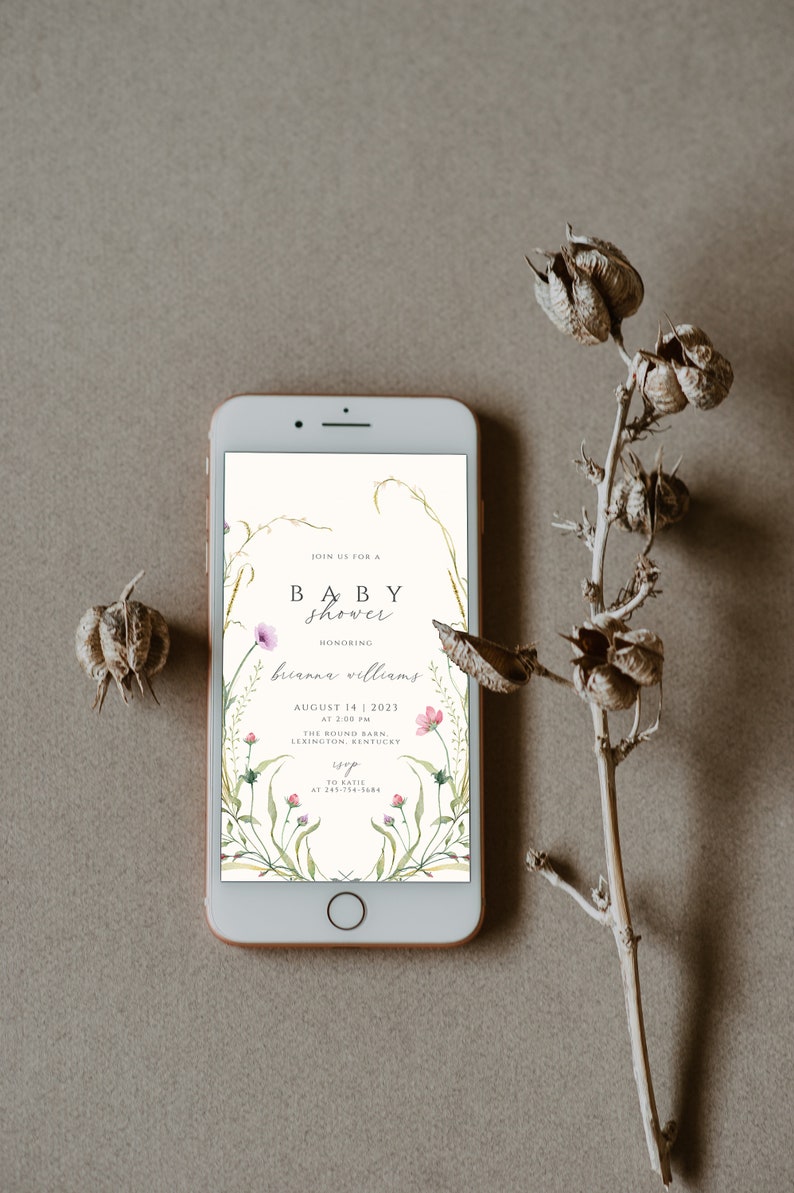 May include: A digital invitation on a smartphone screen for a baby shower. The invitation features a floral design with pink flowers and green leaves. The text reads "Join us for a baby shower honoring Brianna Williams, August 14, 2023 at 2:00 PM, The Round Barn, Lexington, Kentucky. RSVP to Katie at 245-754-5684."