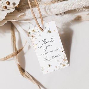 K&ouml;nnte beinhalten: Wei&szlig;es Dankesch&ouml;n-Etikett mit Blumenmuster und Bienen. Das Etikett lautet "Danke, dass du hier bist!" mit einer handschriftlichen Unterschrift.