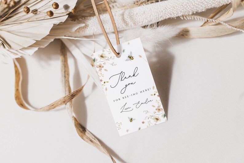 K&ouml;nnte beinhalten: Wei&szlig;es Dankesch&ouml;n-Etikett mit Blumenmuster und Bienen. Das Etikett lautet "Danke, dass du hier bist!" mit einer handschriftlichen Unterschrift.