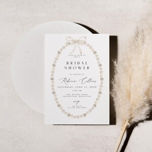 May include: A white bridal shower invitation featuring a pearl necklace design. The text reads "Please join us for a Bridal Shower in honour of Rebecca Collins, Saturday, June 11, 2022, 1:00 PM, The Round Barn, Lexington, Kentucky."