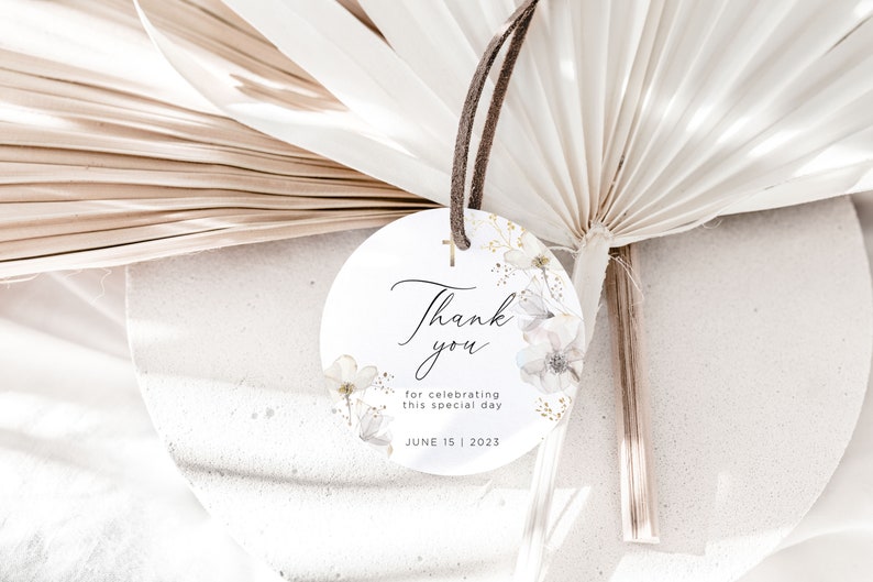 Puede incluir: Una etiqueta redonda y blanca con las palabras "Thank you" en escritura elegante, adornada con ilustraciones florales y una peque&ntilde;a cruz dorada. La etiqueta incluye el texto "for celebrating this special day" y la fecha "JUNE 15 | 2023". Una cuerda marr&oacute;n est&aacute; adjunta.
