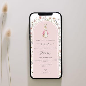 Op de afbeelding: Een roze en witte digitale uitnodiging met een bloemige rand. De uitnodiging bevat een aquarel-illustratie van een konijn dat een roze jurk draagt. De tekst luidt "Some bunny is turning one. Please join us to celebrate Blake's 1st Birthday. Saturday, December 17, 2022. 1:00 PM. The Round Barn, Elsmoore, Kentucky."