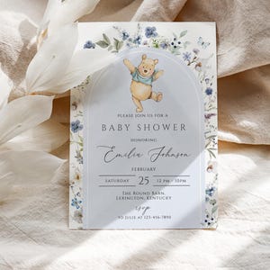 May include: A baby shower invitation featuring a watercolor illustration of Winnie the Pooh. The invitation includes the text "PLEASE JOIN US FOR A BABY SHOWER HONORING Emilia Johnson" and event details. Floral and butterfly accents frame the text.