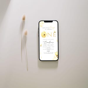 Może przedstawiać: Smartfon wyświetlający zaproszenie na pierwsze urodziny z motywem pszcz&oacute;ł. Zaproszenie przedstawia plaster miodu z pszczołą i cyfrą "jeden" w złotych literach. Tekst brzmi "Our little bee is turning one" i "Emilias First Bee-Day".