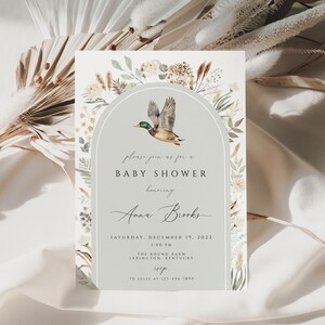 May include: A light blue baby shower invitation with a watercolor illustration of a duck flying in an archway of greenery. The text reads "Please join us for a Baby Shower honoring Anne Banks Saturday, December 19, 2022 1:00 PM The Round Barn Lexington, Kentucky RSVP"