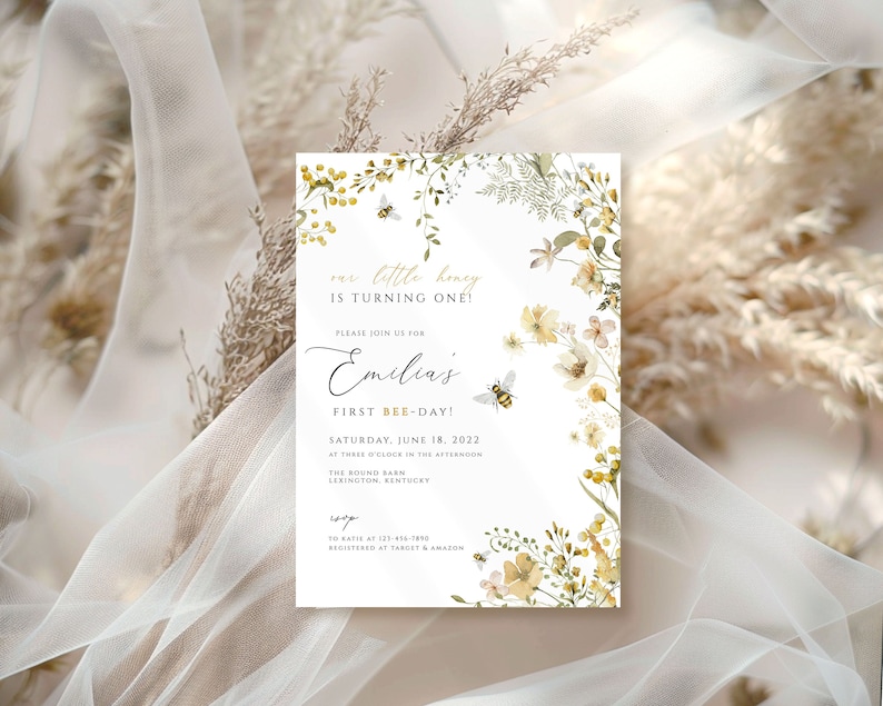 K&ouml;nnte beinhalten: Eine wei&szlig;e Einladungskarte mit einem floralen Design mit gelben Blumen, gr&uuml;nen Bl&auml;ttern und einer Biene. Der Text auf der Karte lautet "our little honey is turning one!" und "Emilia's First Bee-Day!" Das Datum und die Uhrzeit der Veranstaltung sind mit "Saturday, June 18, 2022 at three o'clock in the afternoon" angegeben. Der Ort ist mit "The Sound Barn, Lexington, Kentucky" angegeben.
