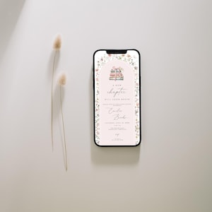 May include: A digital invitation on a smartphone screen with a floral border. The invitation features a stack of books with a pink ribbon and the text "A new chapter will soon begin". The invitation is for a baby shower for a baby named "Colin Brooks".