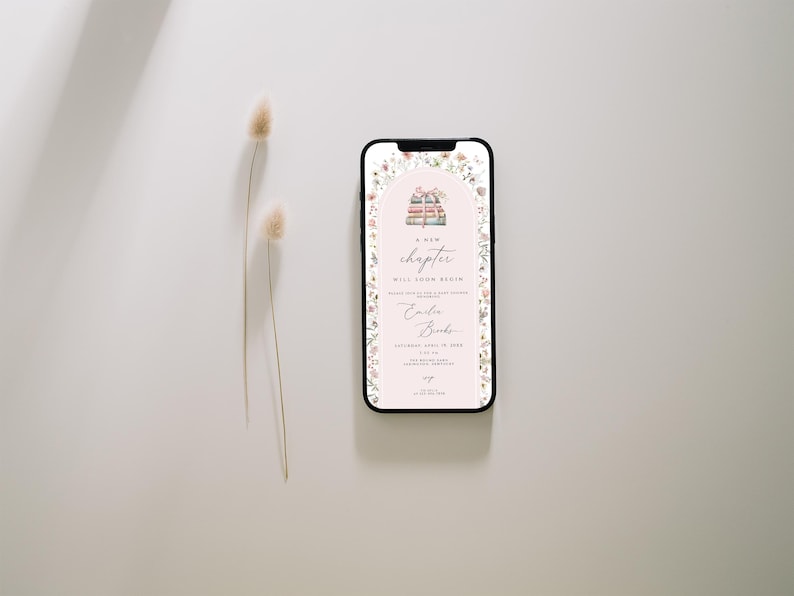 May include: A digital invitation on a smartphone screen with a floral border. The invitation features a stack of books with a pink ribbon and the text "A new chapter will soon begin". The invitation is for a baby shower for a baby named "Colin Brooks".