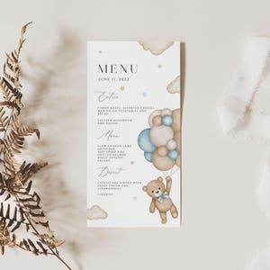 May include: A menu card featuring a charming teddy bear holding blue and beige balloons. The menu card displays the text "MENU" at the top and the date "JUNE 15, 2023". The menu is divided into sections labelled "Entree", "Main", and "Dessert".