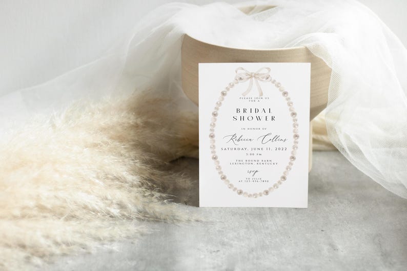May include: A white bridal shower invitation featuring a pearl necklace and bow design. The text reads "Please join us for a Bridal Shower in honour of Rebecca Collins, Saturday, June 11, 2022, 2:00 PM, The Round Barn, Lexington, Kentucky, RSVP at 123-456-7890."