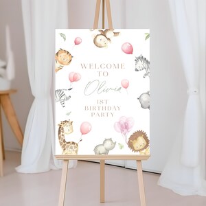 May include: Welcome to Olivia's 1st Birthday Party sign with a jungle animal theme. The sign features a giraffe, zebra, lion, monkey, and hippo with pink balloons.