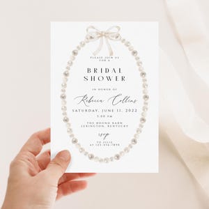 May include: A white bridal shower invitation featuring a pearl necklace and bow illustration. The text reads "Please join us for a Bridal Shower in honour of Rebecca Collins, Saturday, June 11, 2022, 1:00 PM, The Round Barn, Lexington, Kentucky, RSVP to Julie at 123-456-7890."