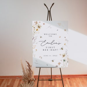 K&ouml;nnte beinhalten: Ein wei&szlig;es Schild mit Aquarell-Blumenillustrationen und Bienen. Das Schild lautet "Willkommen zu Emilias erstem Bienentag! 11. Juni 2022".