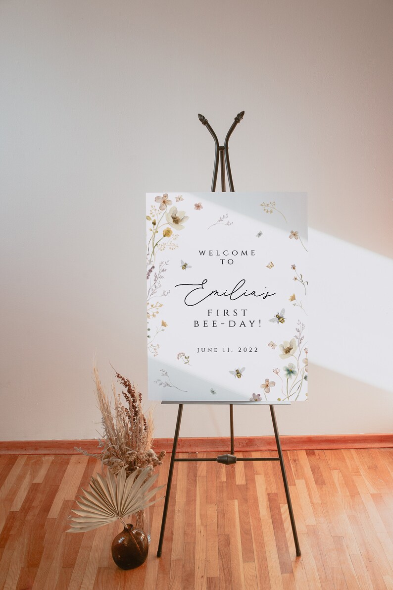 K&ouml;nnte beinhalten: Ein wei&szlig;es Schild mit Aquarell-Blumenillustrationen und Bienen. Das Schild lautet "Willkommen zu Emilias erstem Bienentag! 11. Juni 2022".