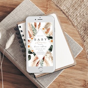 May include: A digital invitation on a smartphone screen for a baby shower. The invitation features a floral design with pampas grass, eucalyptus leaves, and white daisies. The text on the invitation reads "Join us for a Baby Shower Honoring [name] January 28, 2023 at 2:00 PM [address]"