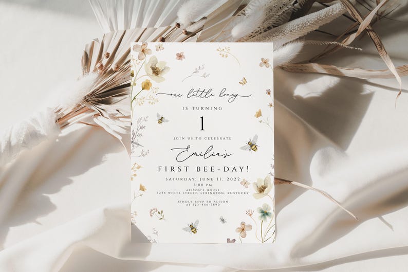 May include: A white invitation card with a floral design and the text "one little bug is turning 1. Join us to celebrate Emilia's First Bee-Day! Saturday, June 11, 2022 1:00 PM Allison's House 1234 White Street, Lexington, Kentucky RSVP to Allison at 123-456-7890"