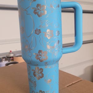 Puede incluir: Una taza de viaje de acero inoxidable azul claro con asa. La taza tiene un dise&ntilde;o plateado de Stitch de Lilo & Stitch y flores de hibisco.