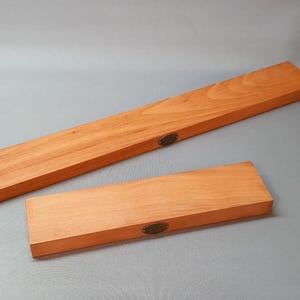 May include: Two wooden rectangular display shelves with a natural wood finish. The shelves have a small brass plaque on the front.