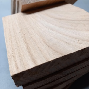 Può includere: Una pila di assi di legno di colore chiaro con venature visibili. Le assi sono rettangolari e sembrano appena tagliate. Il legno ha un aspetto naturale, non rifinito, con variazioni di colore e consistenza.