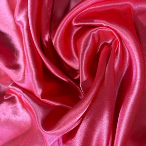 May include: A close-up shot of a vibrant pink satin fabric. The fabric is draped and folded, creating a swirling pattern with highlights and shadows. The material has a smooth, shiny texture.