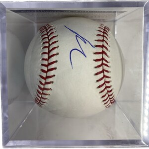 May include: A white baseball with red stitching and a blue signature, encased in a clear acrylic display case. The baseball is a standard size, showcasing the classic design and stitching details.