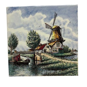 May include: Square ceramic tile featuring a picturesque Dutch landscape. The image depicts a traditional windmill with a thatched roof, a bridge, and a small boat on a canal. The sky is cloudy, and the scene is filled with trees and greenery.