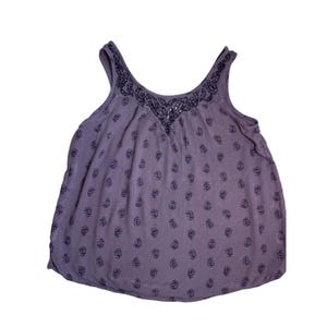 May include: A sleeveless, lavender tank top with a V-neckline and a floral pattern. The neckline and upper chest area feature a detailed, dark blue embroidered design. The fabric has a soft, flowing appearance.