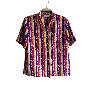 May include: A short-sleeved button-down shirt with a vibrant vertical pattern of purple, yellow, and white wavy stripes. The shirt has a classic collar and is hanging on a white hanger. The fabric appears to be lightweight.