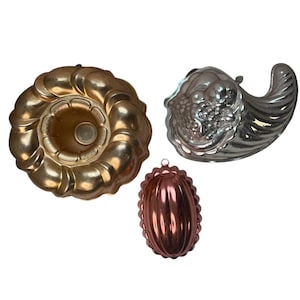 Puede incluir: Tres moldes de metal vintage para hornear o decorar. Incluye un molde para bizcocho dorado, una cornucopia plateada y un pequeño molde ovalado de color cobre. Cada molde tiene un lazo para colgar.
